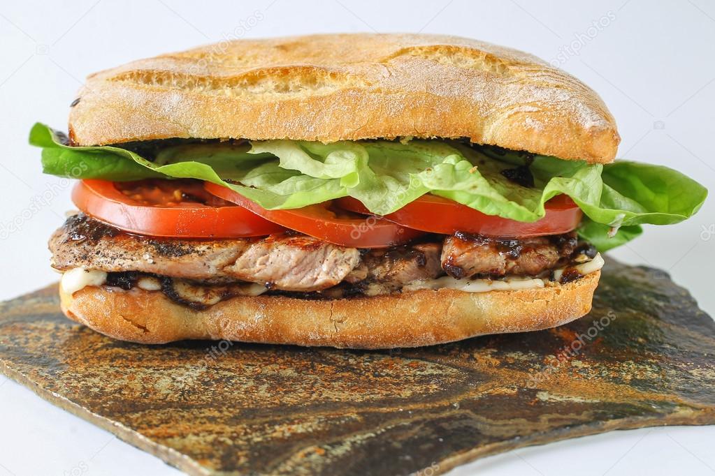 Tasty pork steak sandwich in a ciabatta with tomatos, lettuce