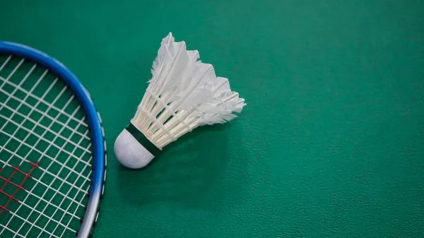 Yeşil bir mahkeme yüzeyi üzerinde badminton raketine yerleştirilmiş beyaz bir mekik siki detaylı bir yakın plan, hassasiyeti, çevikliği ve oyuna odaklanmayı sembolize eder..