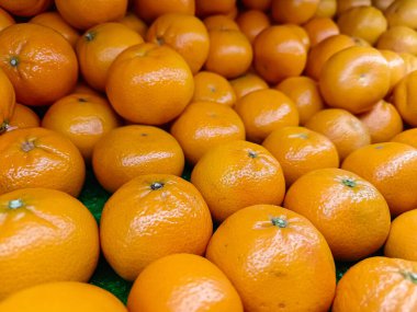 Çerçeveyi dolduran yoğun ve renkli taze toplanmış parlak turuncu portakal (mandalina) yığınını yakına çeken bir makro çekim. Resim, meyvenin parlak dokusunu ve bolluğunu vurgular, narenciye ve sağlıkla ilgili konular için idealdir.