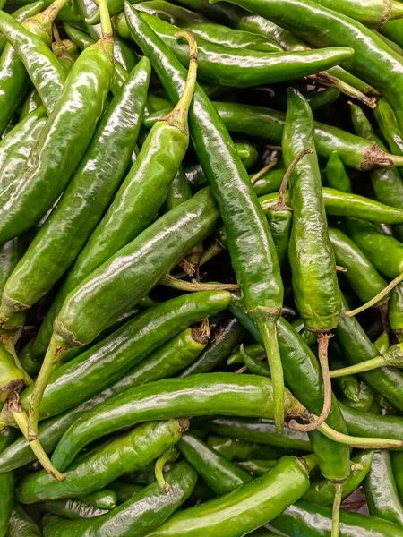 Çerçeveyi dolduran yoğun, uzun yeşil biber yığınını gösteren bir makro yakın çekim. Resim, baharatlı yiyecekler, yemek pişirme, Asya mutfağı ve organik tarım için ideal olan parlak dokuyu, canlı rengi ve ürünlerin sıcaklığını vurguluyor.