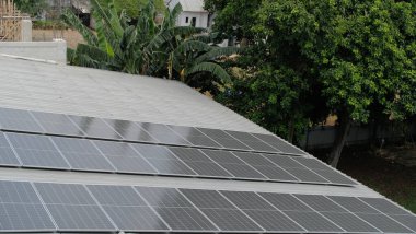 Gri kıvrımlı metal çatıya yerleştirilmiş büyük bir fotovoltaik güneş paneli dizisi. Paneller, temiz, sürdürülebilir ve yenilenebilir enerji teknolojisini sembolize ederek güneş ışığını yakalıyor.