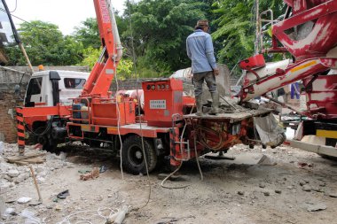 Kauçuk çizmeli inşaat işçileri yeni döşenmiş zemine taze, ıslak beton dökmek için geniş esnek bir pompa borusu kullanıyorlar. Sahne endüstriyel yapı, Jakarta, Aralık 2025 'i vurgular