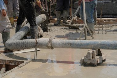 İnşaat işçilerini büyük bir boru ve pompayla bir inşaat sahasının zeminine ıslak, sıvı beton dökerek yakalamak.