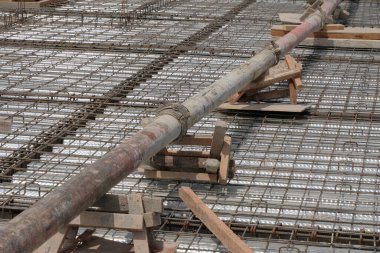Çelik takviye çubuklarının (demir çubuk) bükülmüş metal güverte üzerine döşenmiş bir katman üzerindeki ahşap desteklerin üzerinde duran beton bir pompa borusunun çapraz görüntüsü