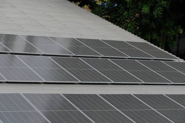 Gri kıvrımlı metal çatıya yerleştirilmiş büyük bir fotovoltaik güneş paneli dizisi. Paneller, temiz, sürdürülebilir ve yenilenebilir enerji teknolojisini sembolize ederek güneş ışığını yakalıyor.