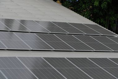 Gri kıvrımlı metal çatıya yerleştirilmiş büyük bir fotovoltaik güneş paneli dizisi. Paneller, temiz, sürdürülebilir ve yenilenebilir enerji teknolojisini sembolize ederek güneş ışığını yakalıyor.