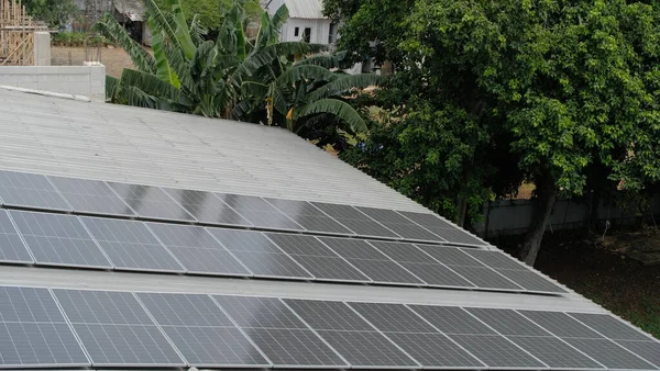 Gri kıvrımlı metal çatıya yerleştirilmiş büyük bir fotovoltaik güneş paneli dizisi. Paneller, temiz, sürdürülebilir ve yenilenebilir enerji teknolojisini sembolize ederek güneş ışığını yakalıyor.