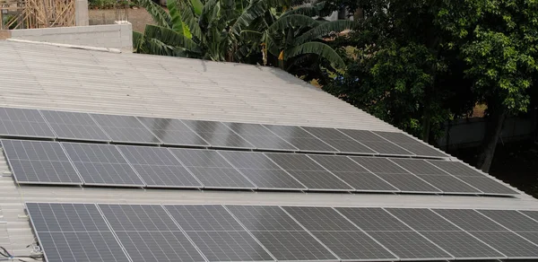 Gri kıvrımlı metal çatıya yerleştirilmiş büyük bir fotovoltaik güneş paneli dizisi. Paneller, temiz, sürdürülebilir ve yenilenebilir enerji teknolojisini sembolize ederek güneş ışığını yakalıyor.