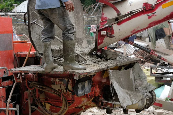 Kauçuk çizmeli inşaat işçileri yeni döşenmiş zemine taze beton dökmek için geniş esnek bir pompa borusu kullanıyorlar.