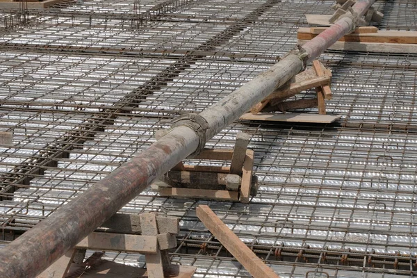 Çelik takviye çubuklarının (demir çubuk) bükülmüş metal güverte üzerine döşenmiş bir katman üzerindeki ahşap desteklerin üzerinde duran beton bir pompa borusunun çapraz görüntüsü