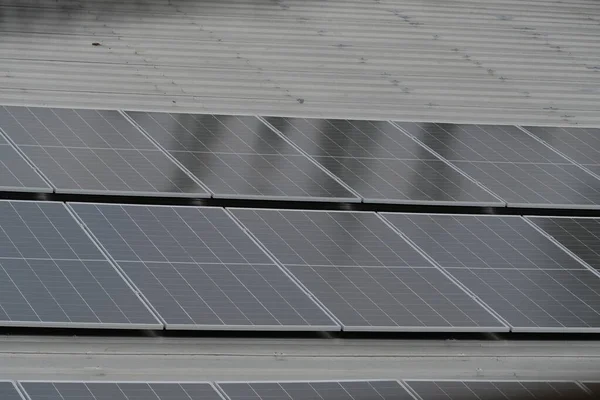 Gri kıvrımlı metal çatıya yerleştirilmiş büyük bir fotovoltaik güneş paneli dizisi. Paneller, temiz, sürdürülebilir ve yenilenebilir enerji teknolojisini sembolize ederek güneş ışığını yakalıyor.