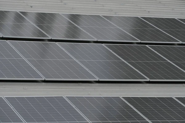 Gri kıvrımlı metal çatıya yerleştirilmiş büyük bir fotovoltaik güneş paneli dizisi. Paneller, temiz, sürdürülebilir ve yenilenebilir enerji teknolojisini sembolize ederek güneş ışığını yakalıyor.