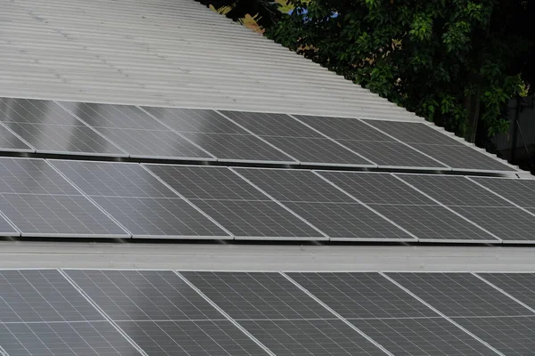 Gri kıvrımlı metal çatıya yerleştirilmiş büyük bir fotovoltaik güneş paneli dizisi. Paneller, temiz, sürdürülebilir ve yenilenebilir enerji teknolojisini sembolize ederek güneş ışığını yakalıyor.