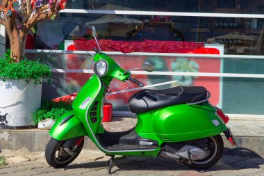 Mobilet. Güzel, yeşil, antika scooter güneşte yıkanmış duruyor. Yazın yeşil motorlu şehir manzarası.