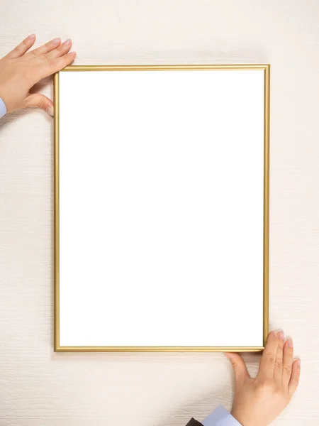 女人把一个模型挂在墙上 年轻女子的手拿着一个金框放在轻墙的背景上 感恩的白色框模型 正方形照片 — 图库照片