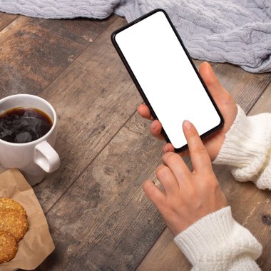 Ahşap masada boş ekranlı siyah cep telefonu tutan bir kadının ellerinin görüntüsü. kare resim