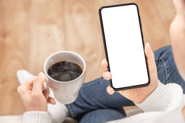 Elinde kahve fincanı olan beyaz ekranlı cep telefonu tutan bir kadının görüntüsü. Cep telefonu Mockup resmi boş beyaz ekran. reklam metni için arkaplan boşluğu