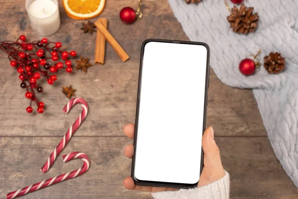 mockup cell phone on background wooden table during the Christmas holidays. woman holds a mobile phone with a blank white screen. Top view. close-up