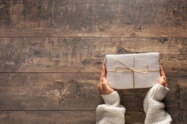 Noel 'i, doğum gününü ya da kırsal ahşap arka planda beyaz kağıda sarılı başka bir kutlama hediyesini elinde tutan genç bir kadının en iyi görüntüsü. Tatil ve kutlamaya hazırlanıyorum. Hediye kutusuna el koyuyorum.