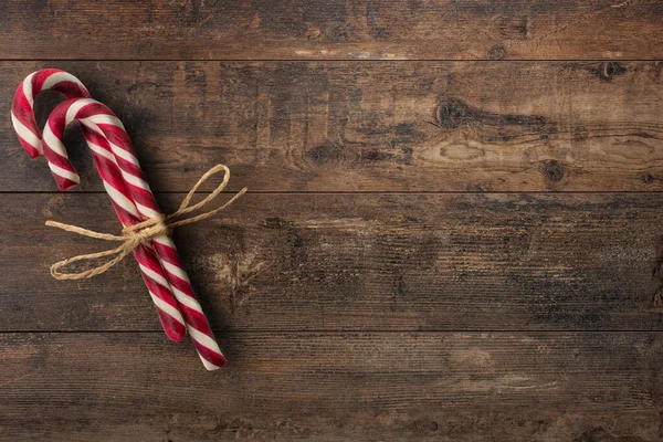 Christmas card with candy canes. Closeup of two candy canes with twine bow on wooden rustic background. Festive minimal style flat lay. For greeting card, invitation.