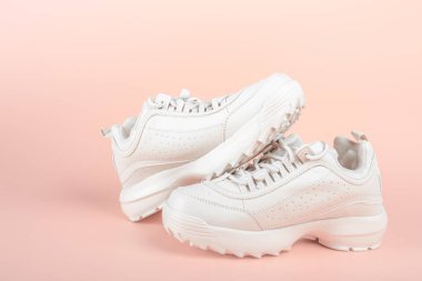 Açık pembe arka planda beyaz spor ayakkabılar. Kadın ayakkabıları. Şık beyaz ayakkabılar. Renkli pastel arka planda modaya uygun beyaz ayakkabılar.