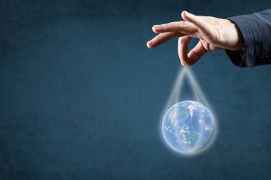 Küreselleşme, Enerji ve ekoloji kavramı. Dünya 'yı iplerle tutan takım elbiseli bir adamın elidir. Mavi arkaplan, kopyalama alanı. Dünyayı oligarklar ve şirketler yönetiyor.