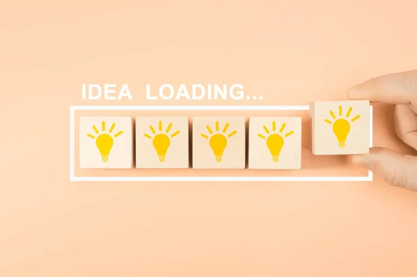 idea loading concept. Hand putting wooden cube block shape with lightbulb. Hand take a wooden cube block with light. Loading bar almost complete with idea beeing processed