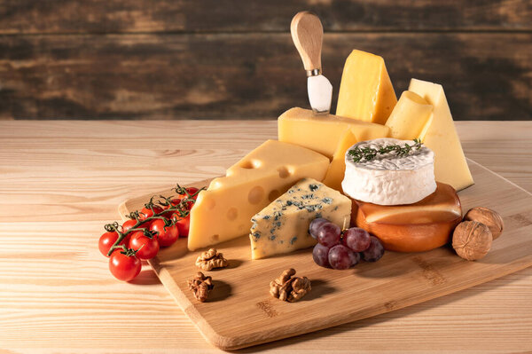 composition different types of cheese with walnuts and grapes on rustic wooden background. blue cheese Dorblu, smoked Suluguni, brie, Maasdam, cheddar, Parmesan.Assortment of different cheese types