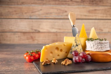 Kırsal ahşap masada çeşitli peynir türleri. Peynir tabağı: parmesan, çedar, gouda, camembert, fındıklı krem peynir, tahta tahta tahtada, koyu arkaplanda yazı için yer var. Lezzetli aperatifler. Boşluğu kopyala.