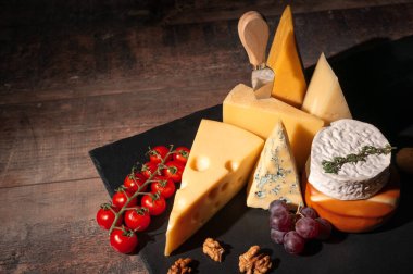 Kırsal ahşap masada çeşitli peynir türleri. Peynir tabağı: parmesan, çedar, gouda, camembert, fındıklı krem peynir, tahta tahta tahtada, koyu arkaplanda yazı için yer var. Lezzetli aperatifler. Boşluğu kopyala.