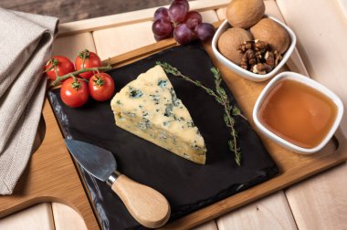 Kahvaltı için ahşap tepsi, mavi peynir, bal, ceviz, domates. Tahta tepside siyah tabakla peynirli kahvaltı.