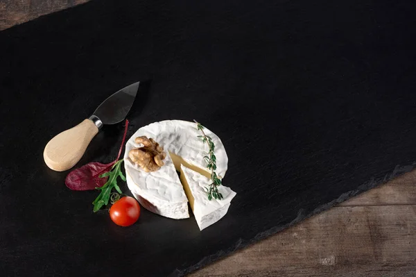 Delicious brie cheese with tomato and walnut on black background and rustic wooden table. Brie type of cheese. Camembert. Fresh Brie cheese and a slice on stone board. Italian, French cheese. top view