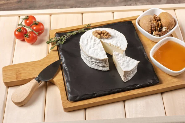 wooden tray for breakfast with brie cheese, honey, walnuts, tomato. cheese breakfast on the wooden tray with black plate