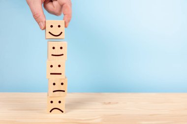 Müşteri hizmetleri değerlendirmesi ve memnuniyet araştırması konseptleri. Müşterinin eli, gülen surat sembolünü tahta bloklarda mavi arka planda seçti. kopyalama alanı. İnceleme, Derecelendirme, Memnuniyet kavramları