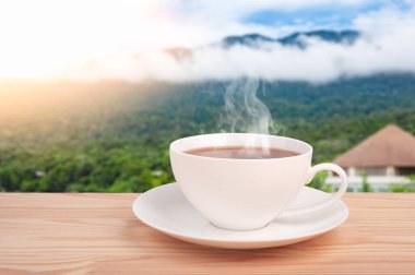 Dağda çay fincanı. Tahta masada organik çay yaprağı ve çay tarlaları. Dağların tepesinde çay fincanı ve güneş ışığı.