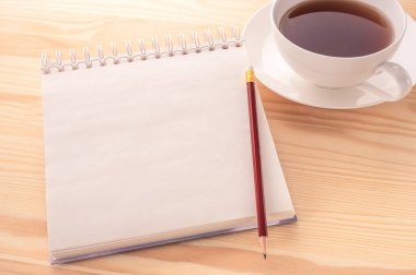 Model görüntüsü. Boş sayfa defterini aç. Fotokopi alanı ve beyaz ahşap masa arkasında bir fincan çay olsun. Boş bir defter, kırmızı bir kalem ve bir fincan çayla ahşap bir masanın üzerinde..