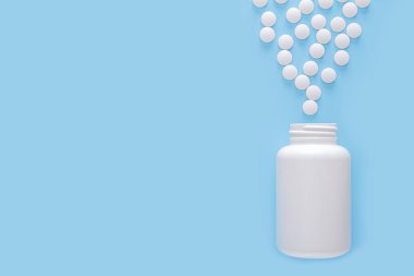 Açık beyaz plastik kavanoz, açık mavi arka planda bir sürü beyaz dağınık hap, tıp konsepti, fotokopi alanı. en üstteki görünüm