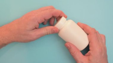 Erkek eli kavanozdan hapları sallar. Mavi arka planda haplar. Haplar şişeden dökülüyor.