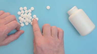Erkek eli kavanozdan hapları sallar. Beyaz, açık plastik bir kavanoz ve beyaz, dağınık haplar.