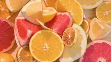 Dilimlenmiş turunçgiller yuvarlak bir tabakta döner. Ahşap arka planda turunçgil meyveleri kesiyor. parlak ışıkta sulu narenciye meyveleri