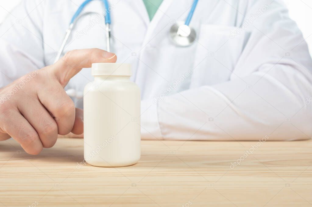 doctor recommends taking medicine, supplement, vitamins, food supplement. Practitioner with bottle of pills. white plastic pill bottle on doctor wooden table. copy space