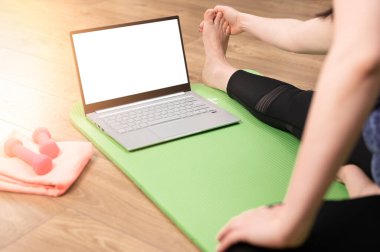 Çevrimiçi ev eğitimi. Kadın evde dizüstü bilgisayarının önünde egzersiz yapıyor, bacaklarını esnetiyor. Kadın evde yoga yapıyor. İnternette bilgisayardan videolar izliyor. Sağlıklı aktif yaşam biçimi