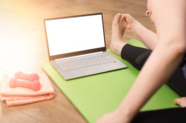 Evde yoga yapan bir kadın dizüstü bilgisayardan video izliyor. Çevrimiçi Laptop Ev Fitness Egzersizi. Kadın dizüstü bilgisayarının önünde egzersiz yapıyor, bacaklarını açıyor.