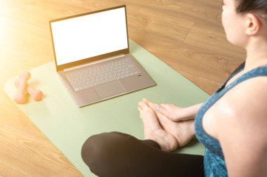 Omzunun üzerinden, dizüstü bilgisayarda laptopun üzerinde yoga eğitimi videosu seyreden sağlıklı bir kadının meditasyon görüntüsü ekrana yansıyor. Uzak çevrimiçi meditasyon öğretim konsepti.