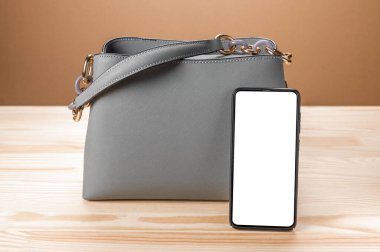 Deri deri deri çanta ve cep telefonlu beyaz ekranlı akıllı kadın. Model görüntüsü. sarı tahta masa arkaplanı