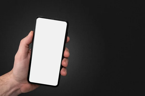 Man hand holding the black cell phone smartphone with blank white screen and modern frame less design on black background. Mockup phone. hand holding mobile phone