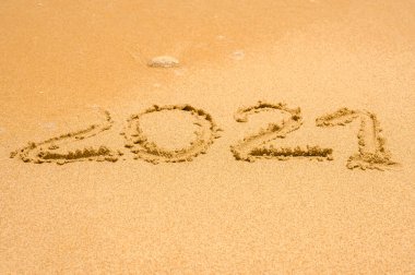 Closeup image of 2021 numbers being washed from wet sand on beach by the sea wave. Concept of recovery of tourism, travel and recreation after the covid 19 pandemic. copy space