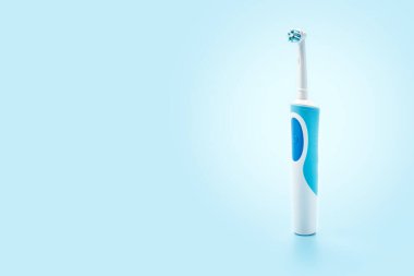 Elektrikli diş fırçası mavi arka planda dikiliyor. Beyaz arka planda diş bakımı araçları. Ağız temizliği kavramı. Elektrikli diş fırçası, yakın plan. Boşluğu kopyala
