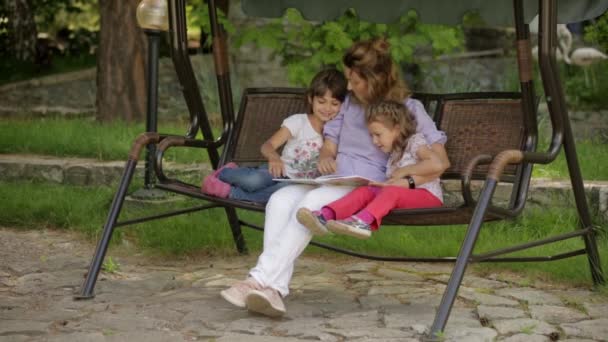 Anne parkta oturan çocuklar için bir kitap okuma — Stok video