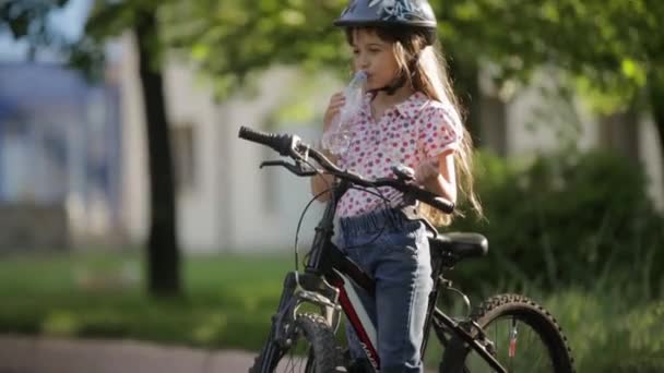 Niña bebe agua mientras está parada en la bicicleta — Vídeo de stock